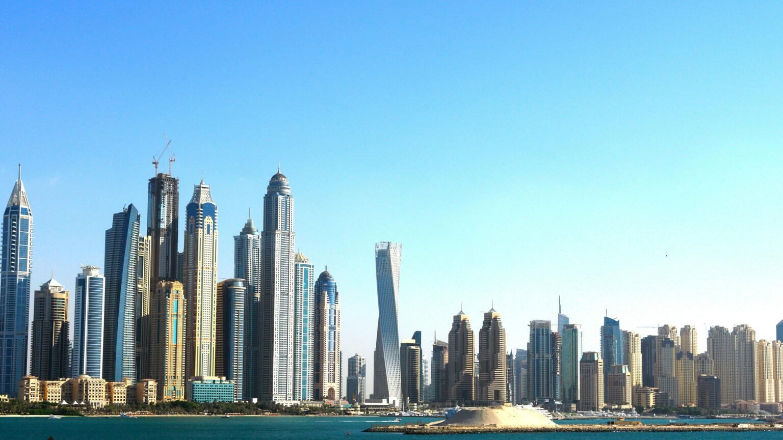 Panoramic view of Dubai's towering skyscrapers set against a vibrant blue sky and waterfront.